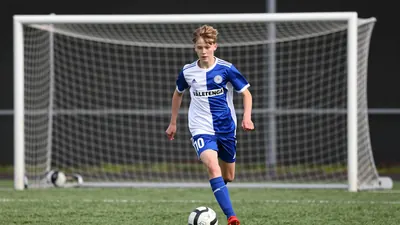 A tight action shot of a 15-year-old player in a Vålerenga Fotball jersey, number 10, with a blue and white kit, running...