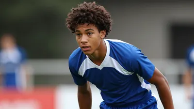 A 18-year-old, dark-skinned player with a messy afro, wearing a blue and white jersey with a white collar, and blue...