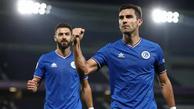 Photorealistic shot of a 31-year-old midfielder in a royal blue football kit, waist-up, celebrating with a fist pump