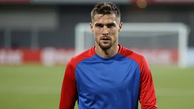Mid-30s male footballer, athletic build, waist-up, wearing an unmarked Vålerenga home training top split blue left side...