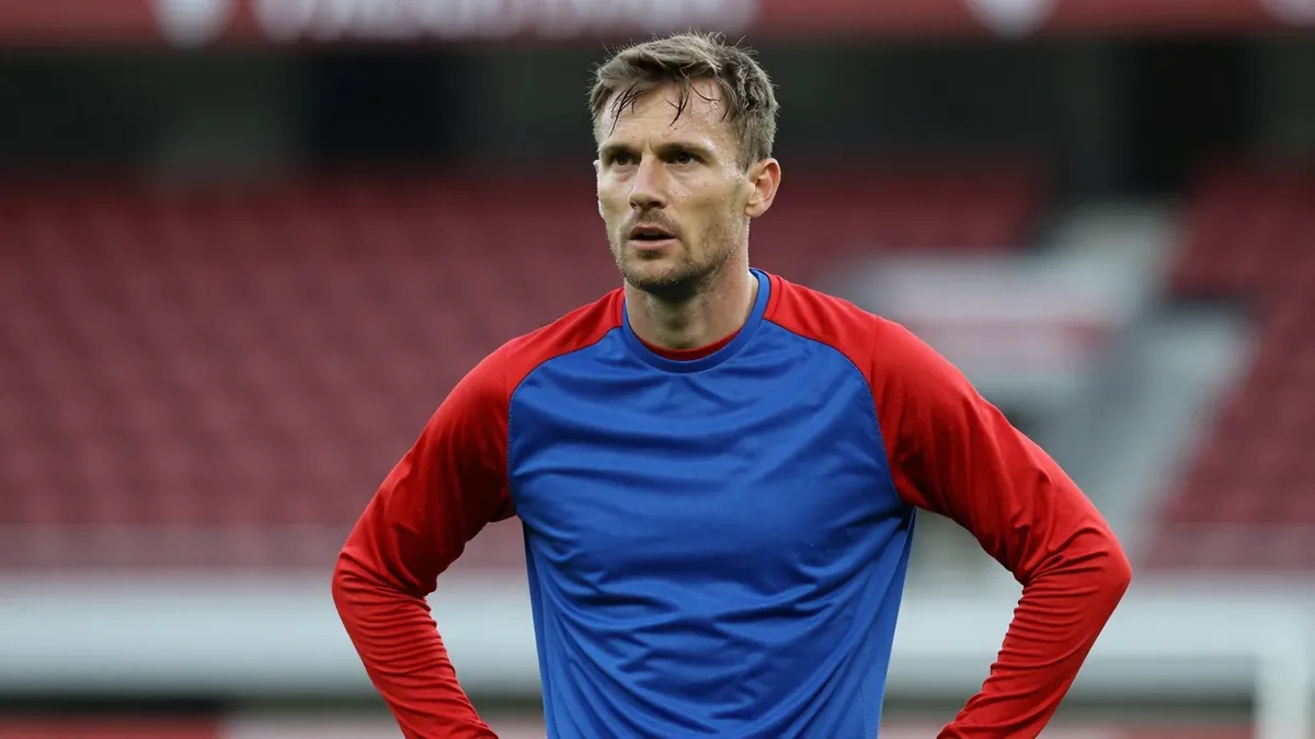 A Vålerenga midfielder in his early 30s, wearing a plain blue and red training top with clean fabric texture, stands...