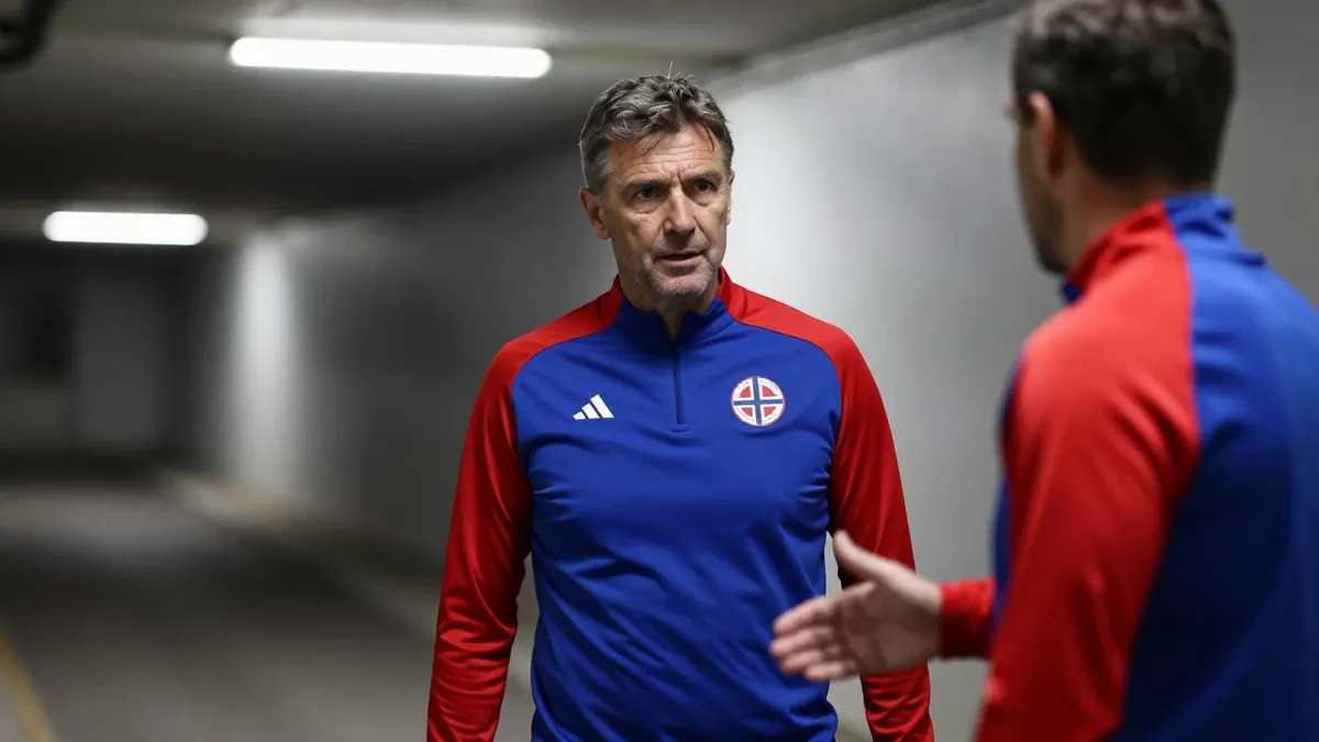 A 50-year-old Norwegian football coach in a plain blue and red Vålerenga training top, stands in the low-lit tunnel at...